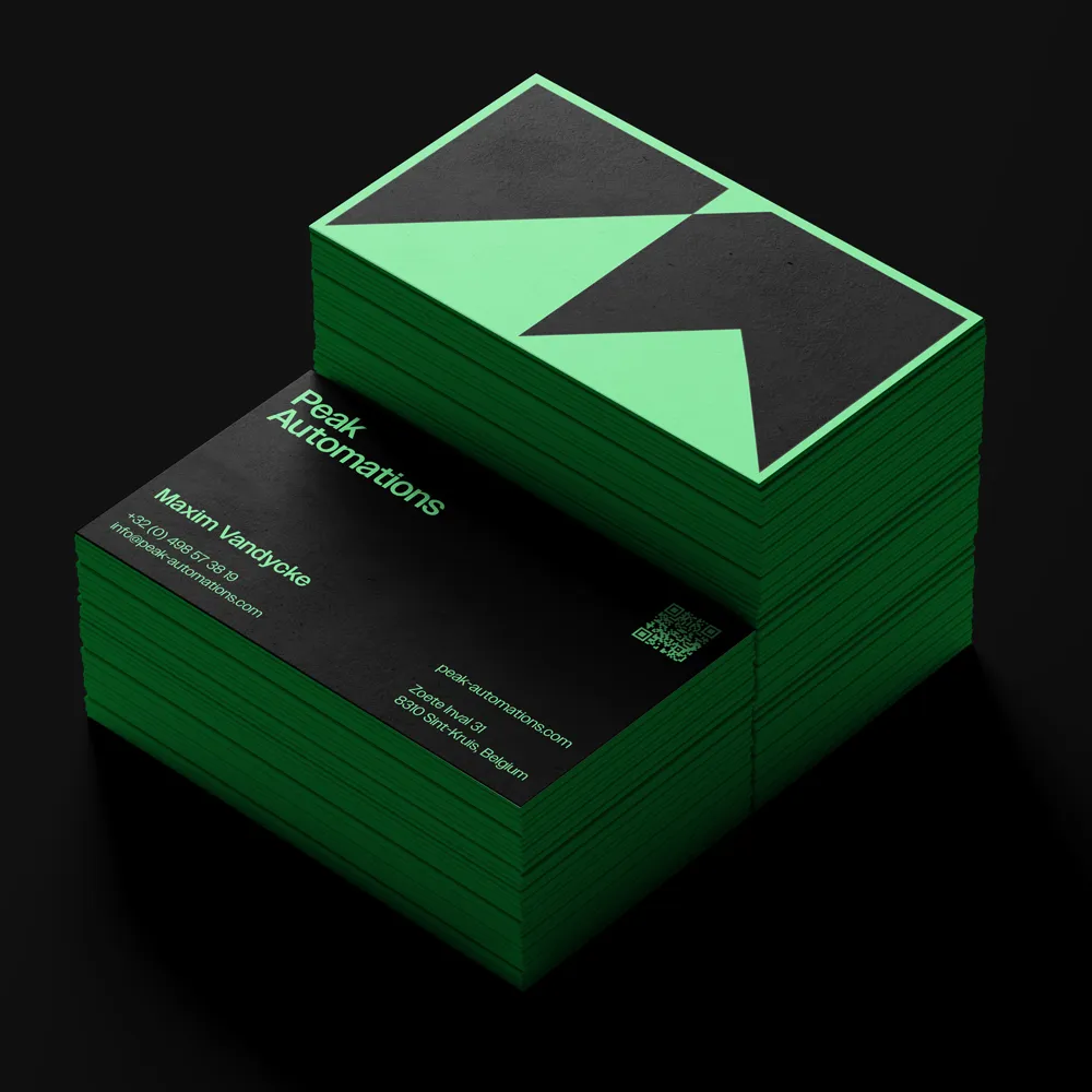 Stack of black and green business cards for Peak Automations with contact details for Maxim Vandycke and a geometric logo.