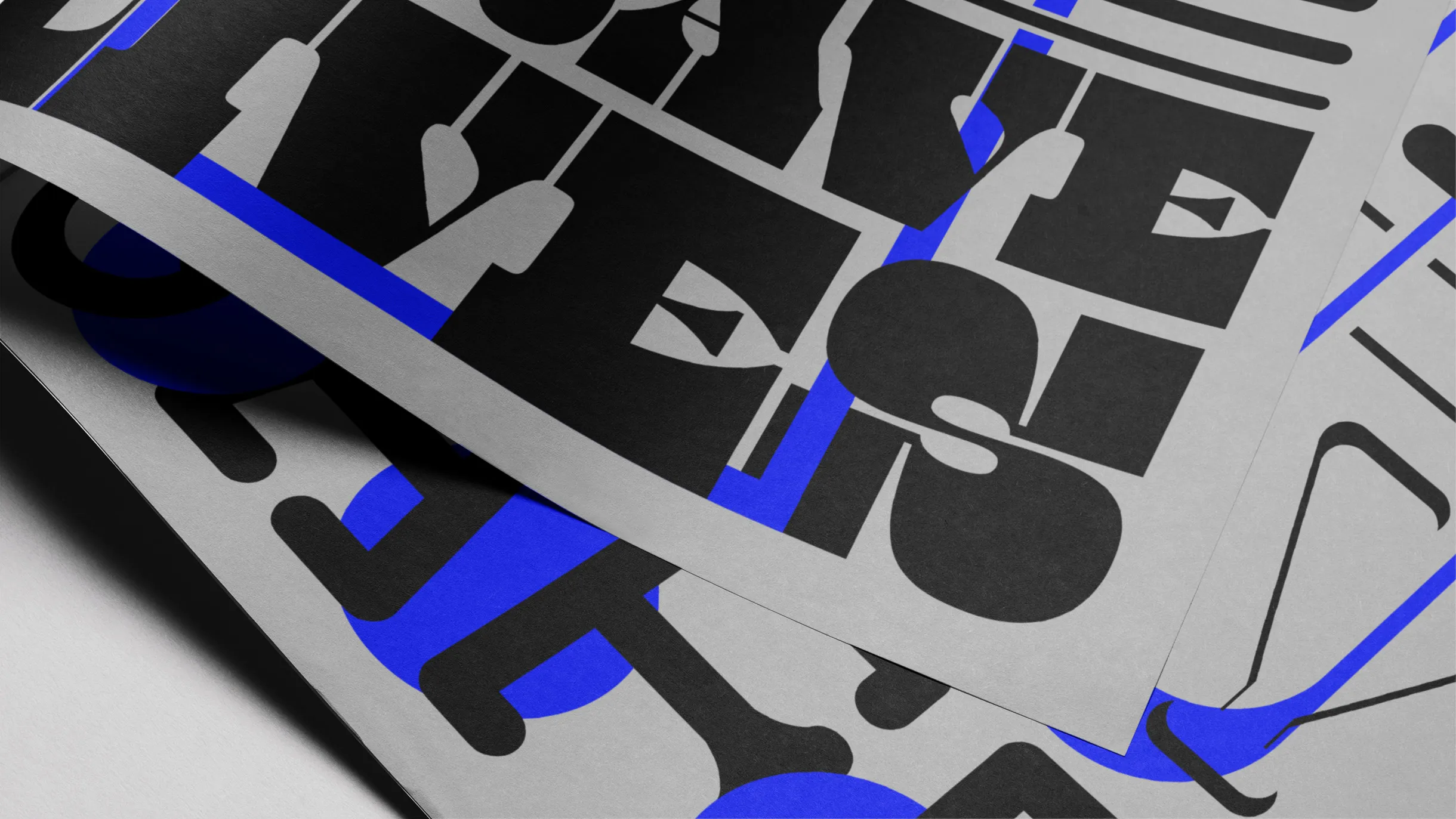 Close-up of overlapping gray sheets with bold black and blue abstract geometric shapes and typography.
